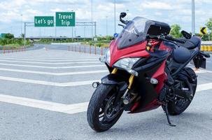 rood zwart motorfiets modern stijl geparkeerd Aan weg met bericht laten we Gaan reizen reis Aan groen verkeersbord achtergrond foto