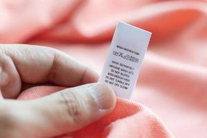 hand- houden en lezing Bij wit wasserij zorg het wassen instructies kleren etiket Aan roze overhemd foto