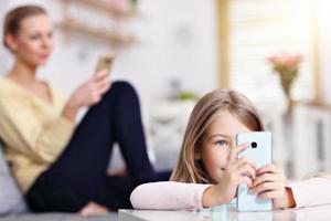 jong mam en haar weinig dochter gebruik makend van smartphone en zittend Aan sofa Bij huis foto