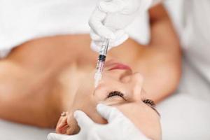 dichtbij omhoog van handen van schoonheidsspecialist maken botox injectie in vrouw lippen foto