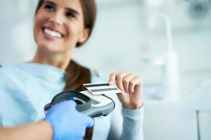 volwassen vrouw betalen voor bezoek in tandarts kantoor foto