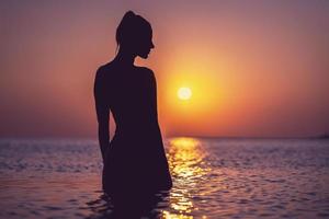 silhouet van jong vrouw beoefenen yoga Aan de strand Bij zonsopkomst foto