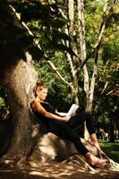 jong vrouw zittend Aan een boom en lezing foto