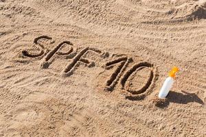 zon beschermen factor tien. spf 10 woord geschreven Aan de zand en wit fles met zonnebrand room. huid zorg concept achtergrond foto
