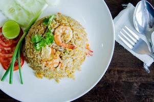 gebakken rijst- met garnaal in een wit schotel Aan hout tafel in Thais voedsel stijl foto
