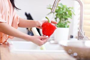 jong vrouw het wassen rood klok peper in modern keuken foto