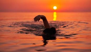 jong vrouw zwemmen in de zee Aan zonsopkomst foto