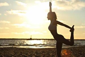 silhouet jonge vrouw beoefenen van yoga op het strand bij zonsondergang foto