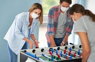 paar van studenten vervelend maskers spelen tafel voetbal in de campus foto