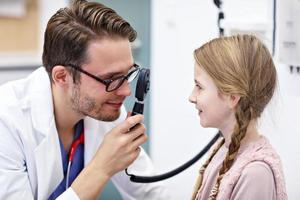 kind mannetje optometrist onderzoekt gezichtsvermogen van weinig meisje foto