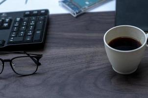 houten bureau met een kop van koffie, een bril, computer toetsenbord en een boek. concept foto over kantoor bureau