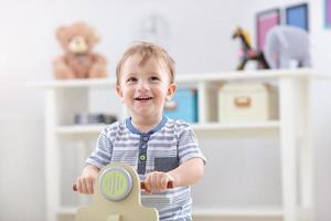 vrolijk baby jongen swinging Aan een schommelen stoel in de vorm van een scooter foto