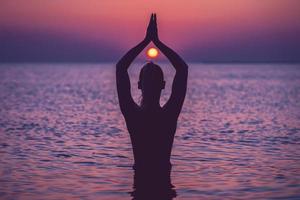 silhouet van jong vrouw beoefenen yoga Aan de strand Bij zonsopkomst foto