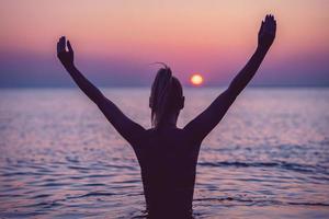 silhouet van jong vrouw beoefenen yoga Aan de strand Bij zonsopkomst foto