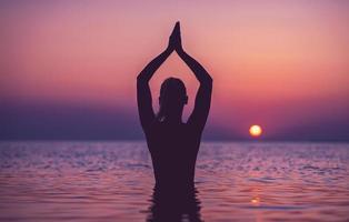 silhouet van jong vrouw beoefenen yoga Aan de strand Bij zonsopkomst foto