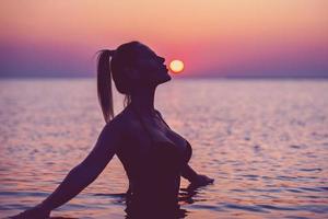 silhouet van jong vrouw beoefenen yoga Aan de strand Bij zonsopkomst foto