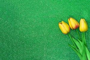 drie geel tulpen Aan groen achtergrond met schittert. groet kaart met Pasen, maart 8, gelukkig verjaardag, moeder dag. kopiëren ruimte foto