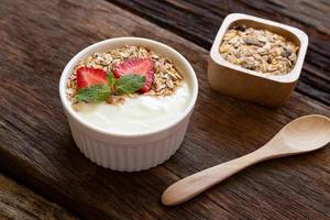 aardbei yoghurt in een houten kom met muesli, honing, munt en vers aardbei Aan houten achtergrond. Gezondheid voedsel concept. foto