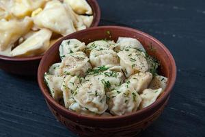 traditioneel Russisch pelmeni of ravioli, knoedels met vlees Aan hout zwart achtergrond. Russisch voedsel en Russisch keuken concept. foto