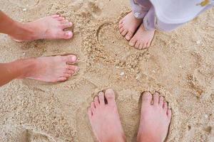 de voeten van een familie, vader, moeder, en kinderen staand Aan de zanderig strand. foto