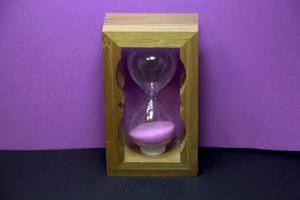 houten roze zand zandloper. klein zand glas foto decoratie geïsoleerd Aan Purper en zwart achtergrond. Nee tekst met ruimte voor kopiëren ruimte.