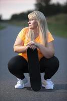 mollig midden- oud Europese vrouw, overgewicht, in een trainingspak met een skateboard, moe na spelen sport, rusten. foto