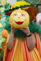 creatief versierd halloween pompoenen in menselijk handen. een soort gezicht met een glimlach geschilderd Aan een pompoen. carnaval kostuum voor de herfst vakantie. foto