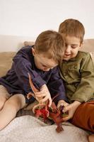 twee weinig en schattig Kaukasisch jongens spelen met dinosaurussen Bij huis. interieur en kleren in natuurlijk aarde kleuren. knus omgeving. kinderen hebben pret met speelgoed, twee vrienden. foto