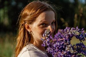 dichtbij omhoog portret van jong mooi roodharige vrouw met sproeten, vervelend wit jurk, poseren in de natuur. meisje met rood haar- Holding bloemen. natuurlijk schoonheid. diversiteit, individu uniciteit. foto