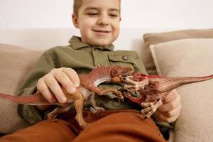 weinig en schattig Kaukasisch jongen spelen met dinosaurussen Bij huis. interieur en kleren in natuurlijk aarde kleuren. knus omgeving. kind hebben pret met speelgoed. foto