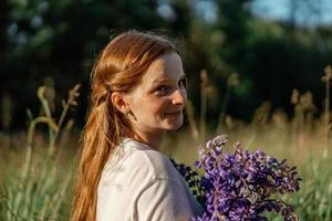 dichtbij omhoog portret van jong mooi roodharige vrouw met sproeten, vervelend wit jurk, poseren in de natuur. meisje met rood haar- Holding bloemen. natuurlijk schoonheid. diversiteit, individu uniciteit. foto