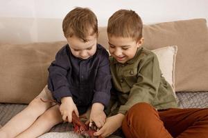 twee weinig en schattig Kaukasisch jongens spelen met dinosaurussen Bij huis. interieur en kleren in natuurlijk aarde kleuren. knus omgeving. kinderen hebben pret met speelgoed, twee vrienden. foto