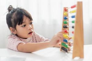 een jong schattig Aziatisch meisje gebruikt het telraam met gekleurde kralen om thuis te leren tellen foto