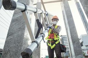 kant visie van arbeider ingenieur in veiligheid helm beklimming de ladder naar krijgen naar de top . arbeider ingenieur metaal dakbedekking werk voor dak. foto