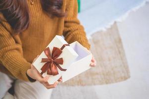 vrolijk Kerstmis en gelukkig vakantie jong vrouw met een mooi gezicht in een geel overhemd shows vreugde met geschenk dozen in een huis met een Kerstmis boom versierd met Kerstmis boom. portret voordat Kerstmis foto