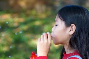 Aziatisch meisje blazen zeep bubbels spelen buitenshuis in de park. concept spelen, speelgoed, kinderen vrije tijd activiteiten. zacht en selectief focus. foto