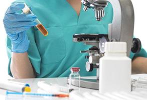 wetenschapper in blauw medisch handschoenen en uniform aan het leren covid-19 monsters met microscoop in laboratorium. foto