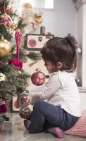 Aziatisch weinig meisje versieren de Kerstmis boom binnenshuis. de ochtend- voordat Kerstmis. portret liefhebbend meisje dichtbij omhoog. foto