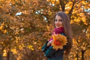 mooi jong meisje staat tegen de backdrop van herfst- bomen en glimlachen foto