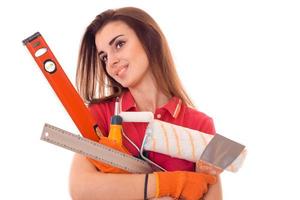 jong vrolijk vrouw met donker haar- in uniform maakt renovaties met gereedschap in haar handen geïsoleerd Aan wit achtergrond foto