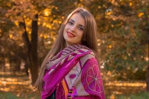 mooi jong meisje in een roze sjaal staat in herfst park en glimlacht foto