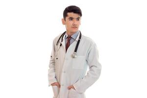 jong elegant brunette dokter in uniform met stethoscoop op zoek weg geïsoleerd Aan wit achtergrond foto