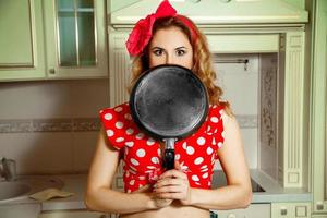 meisje in pin omhoog stijl poseren in de keuken met frituren pan in handen foto
