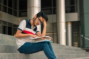 verdrietig jong leerling jongen zit Aan een trap en lezen boek foto