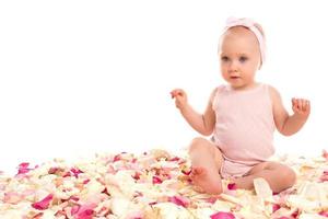 schattig baby meisje zittend omringd roos bloemblaadjes foto