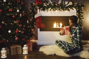 vrouw met een Kerstmis geschenk zittend naast de brand plaats foto