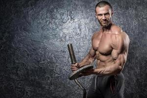 bodybuilder Mens met barbell tegen beton muur foto