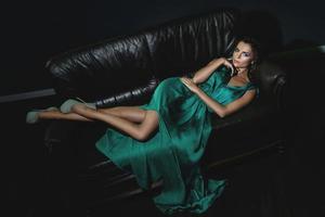 vrouw vervelend mooi groen zijde jurk is poseren Aan leer bankstel foto
