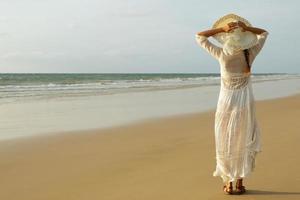 vrouw vervelend mooi wit jurk is wandelen Aan de strand gedurende zonsondergang foto