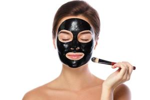 mooi vrouw is toepassen zuiverend zwart masker Aan haar gezicht foto